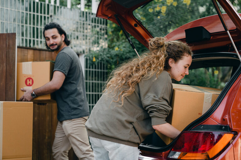A young couple unloads boxes from their vehicle after purchasing a new home under the First Home Buyer Choice Scheme