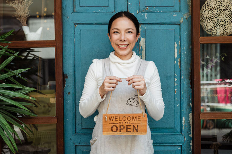 Recognition of Service on Sale and Purchase of Businesses - A woman standing out the front of her business holding an 'Open' sign
